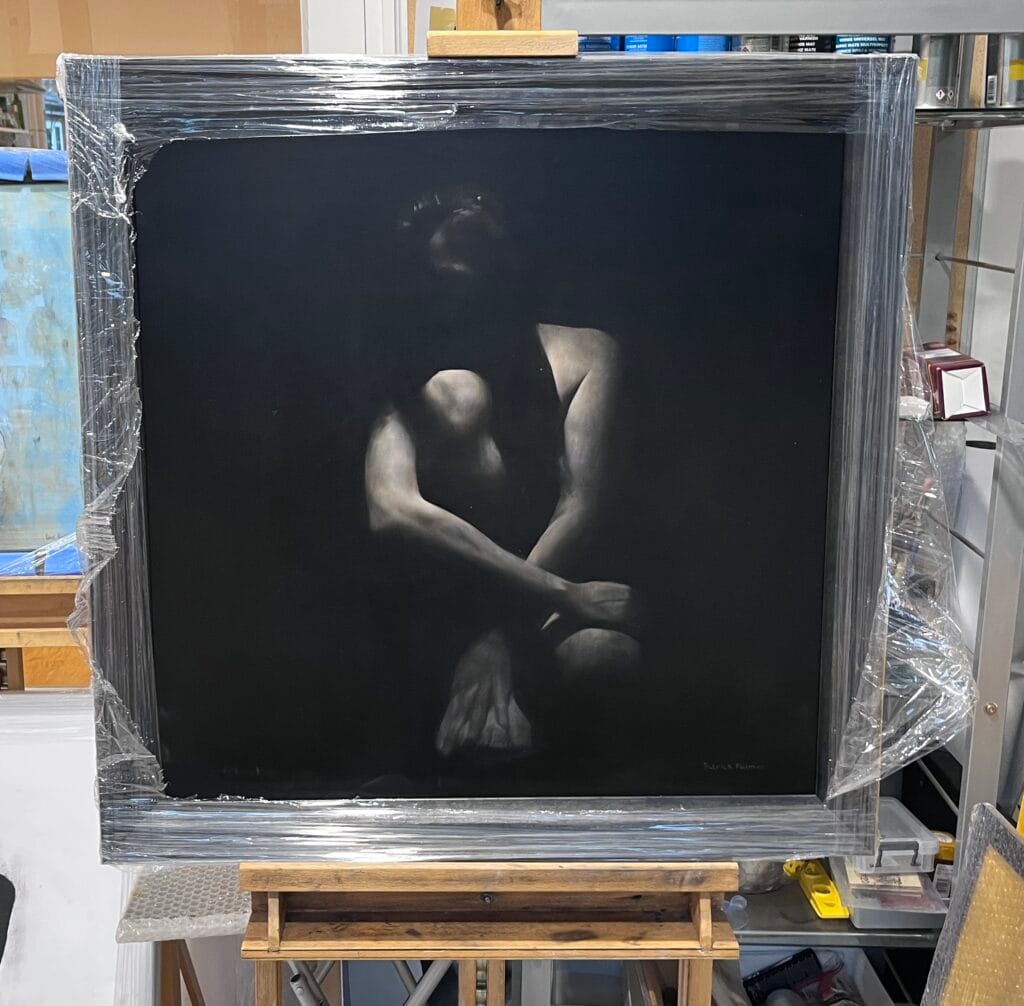 A framed painting of a seated person with their arms crossed over their knees, depicted in dramatic lighting against a dark background. The painting is wrapped in plastic and displayed on an easel in a studio.